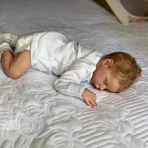 Realistic 18 inch reborn baby doll in white cotton top sleeping on quilted bedding