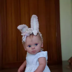 Lifelike 24-inch reborn baby doll with blue eyes, bunny ear headband and white dress