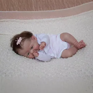 Lifelike 19-inch reborn baby doll with brown hair wearing pink outfit on beige rug