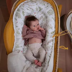 Realistic 18-inch reborn baby doll in pink polka dot outfit resting in a woven basket