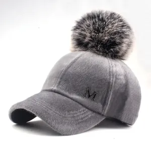 Detail of grey plush baseball cap with faux fur pompom and metal M logo accent