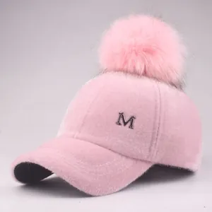 Close-up of pink plush baseball cap with fuzzy pompom and silver metal letter M