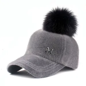 Close-up of grey faux fur winter baseball cap with silver M logo and black pom-pom