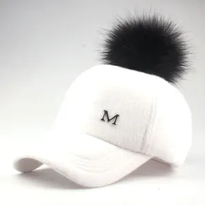 Detailed view of white plush baseball cap featuring a fluffy black faux fur pompom and metal M logo
