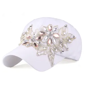 Dettaglio di ricamo floreale dorato con gemme rosa su un cappello bianco da baseball