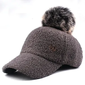 Close-up of grey sherpa baseball cap featuring a fluffy pompom and gold M metal logo