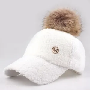 Close-up of fluffy white lamb wool baseball cap with brown faux fur pom pom and golden M logo