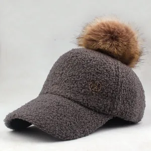 Close-up of winter faux shearling baseball cap with fluffy fur pom and gold M logo
