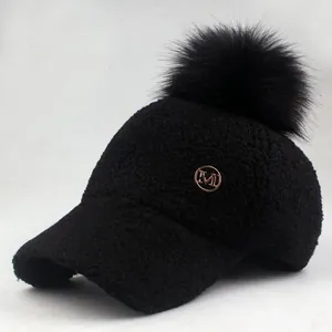 Close-up of black fleece baseball cap with large faux fur pompom and gold M emblem