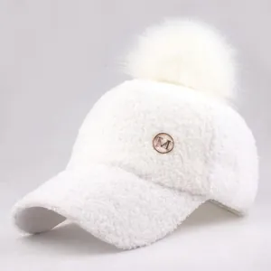 Detail of white sherpa baseball cap featuring a plush pom-pom and metallic M logo