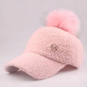 Close-up of pink lamb wool baseball cap with fluffy pom-pom and gold M metal logo