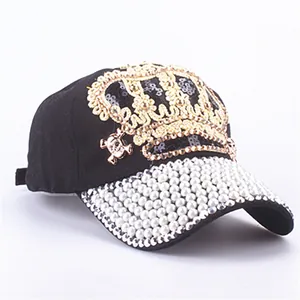 Detail of a black baseball cap featuring a gold crown and pearl embellished brim