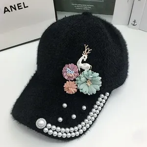 Détail de casquette pelucheuse avec décor floral, cerf doré et perles blanches