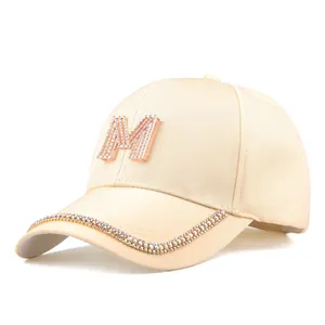 Detail der beigen Baseballkappe mit Strass-M-Logo und funkelnder Verzierung am Schirm