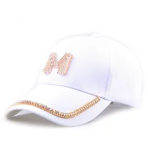 Detailansicht der weißen Baseballkappe mit Strass-M-Logo und glitzernder Krempe