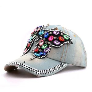 Détail d'une casquette en jean bleu clair avec un grand papillon en strass colorés