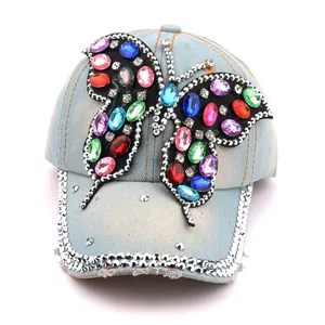 Détail d'une casquette de baseball en jean bleu clair avec un papillon en strass coloré