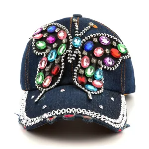 Détail d'une casquette en jean bleu avec papillon en strass colorés et ornements bijoux