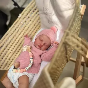 Detail of reborn baby doll LouLou sleeping in a cradle wearing pink knitwear and hat