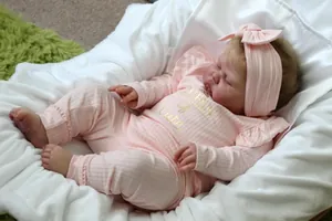 Close-up of lifelike reborn doll wearing a pink ribbed outfit with gold lettering