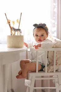 Realistic 60cm reborn baby doll sitting in high chair for first birthday celebration