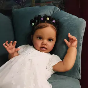 Poupée reborn réaliste 60cm peau foncée, cheveux bouclés et robe dentelle sur sofa