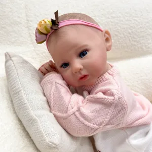 Poupée reborn réaliste de 50cm en pull rose allongée sur un petit coussin blanc texturé