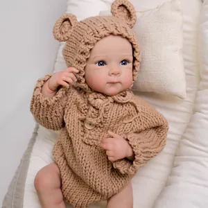 Lifelike 18-inch reborn baby doll wearing a brown knit bear ear romper on white bedding