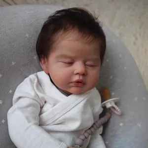 Lifelike 19-inch reborn sleeping baby doll in white outfit with pacifier on grey cushion
