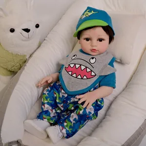Realistic 18-inch reborn baby doll in blue shark outfit resting in a white bassinet