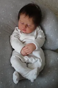 Macro view of lifelike reborn baby doll in white onesie resting on a grey support pillow