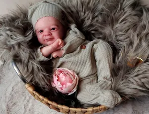 Detail of 18 inch reborn baby doll wearing green knit romper and hat in a cozy cradle