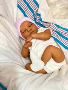 Gros plan d'une poupée reborn Levi endormie à peau foncée avec bonnet rose et body blanc