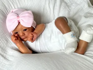 Close-up of a lifelike dark skin reborn baby doll wearing a pink bow hat and white socks