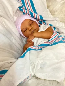 Gros plan d'une poupée reborn endormie à peau foncée avec un bonnet rose sur une couverture