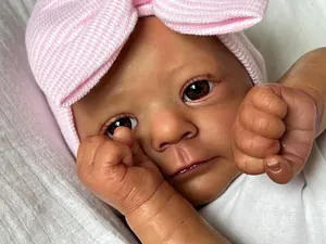 Close-up of a realistic reborn doll featuring brown eyes and a pink bow knit hat