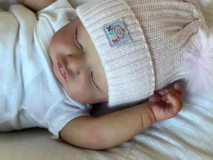 Gros plan d'une poupée reborn endormie avec texture de peau réaliste et bonnet rose