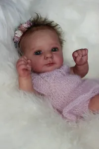 Detailed close-up of 18 inch realistic reborn doll wearing a pink knit romper and floral headband