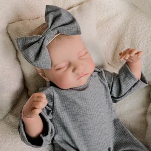 Lifelike 18-inch reborn baby doll wearing a grey romper and bow headband on soft plush