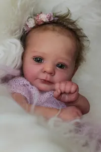 Close-up of a realistic reborn doll with green eyes and a purple knit top for collectors