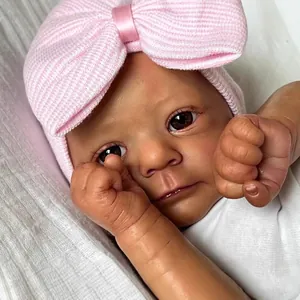 Realistic 18-inch dark skin newborn baby doll wearing a pink knit bow hat and white outfit