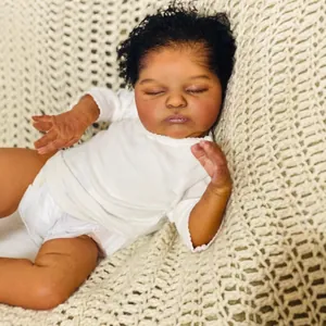 Lifelike 19-inch African baby doll in white romper lying on a beige woven blanket