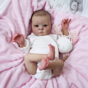 Realistic 16-inch reborn baby doll in white long-sleeved bodysuit on pink plush rug