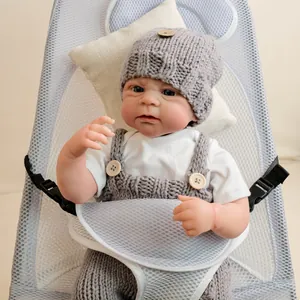 Realistic 19 inch Elijah reborn doll wearing grey knitted overalls and hat in a cradle