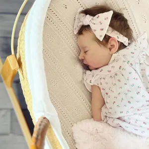 Realistic 19-inch newborn baby doll in floral romper with bow headband in a cradle