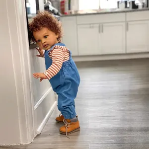 Detail of 26-inch realistic baby doll in denim overalls and brown boots standing at home