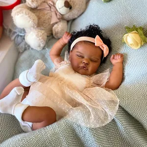 Muñeca Reborn africana durmiendo con vestido blanco sobre manta de punto azul