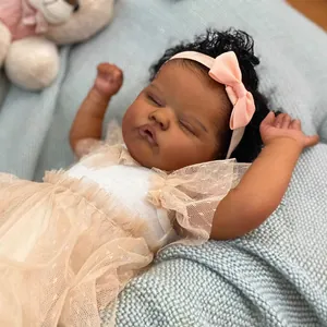 Muñeca Reborn africana de 18 pulgadas con vestido blanco y lazo rosa durmiendo en alfombra azul