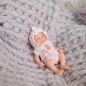 Miniature lifelike pink striped silicone baby doll sleeping on a soft purple blanket