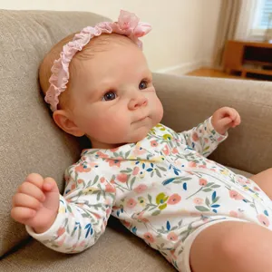 Realistic 19-inch reborn baby doll in floral romper reclining on a grey fabric sofa